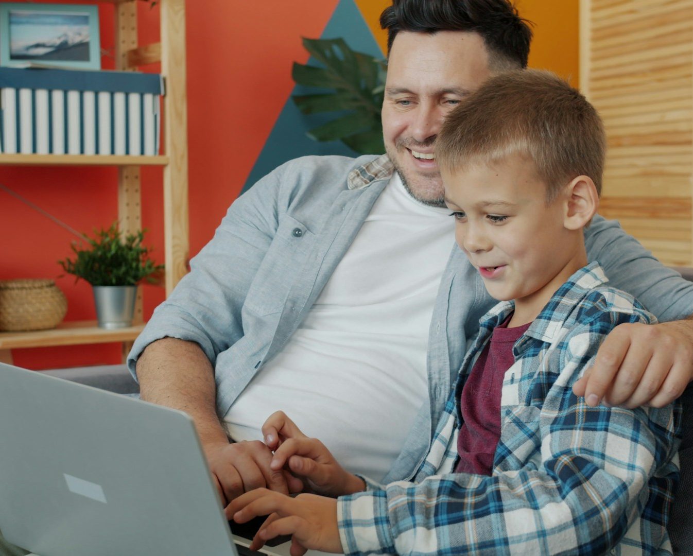 Working on a laptop A father and son enjoy time together while working on a laptop in a cozy setting.